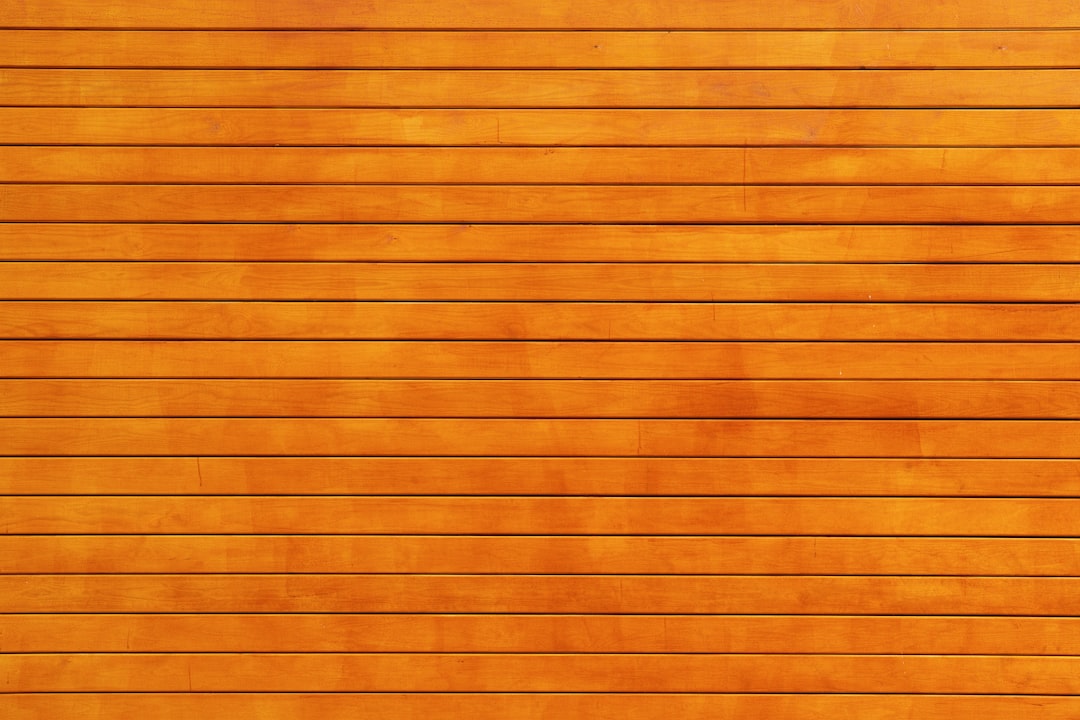 Wooden surface with evenly spaced horizontal slats, stained a warm orange-brown color. The texture of the wood grain is visible, giving the surface a natural and polished appearance.