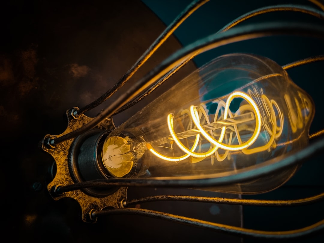 A close-up of a vintage-style light bulb with a glowing spiral filament, surrounded by a metal cage, set against a dark background.