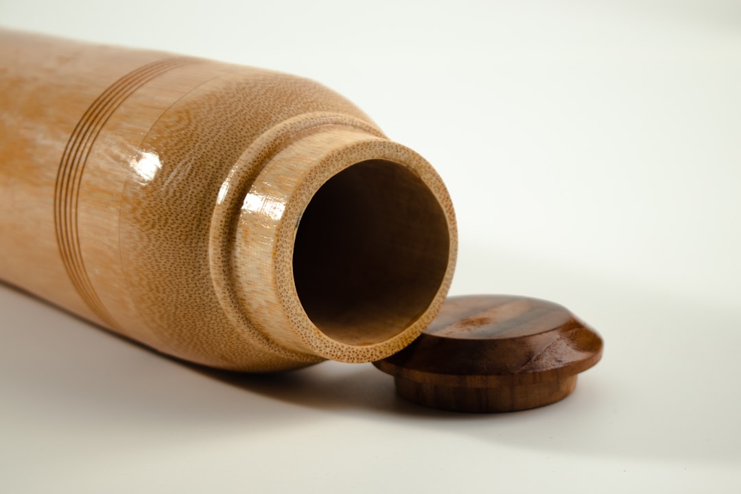 A close-up of a cylindrical wooden container lying on its side with its round lid placed next to the open mouth, on a plain white background.