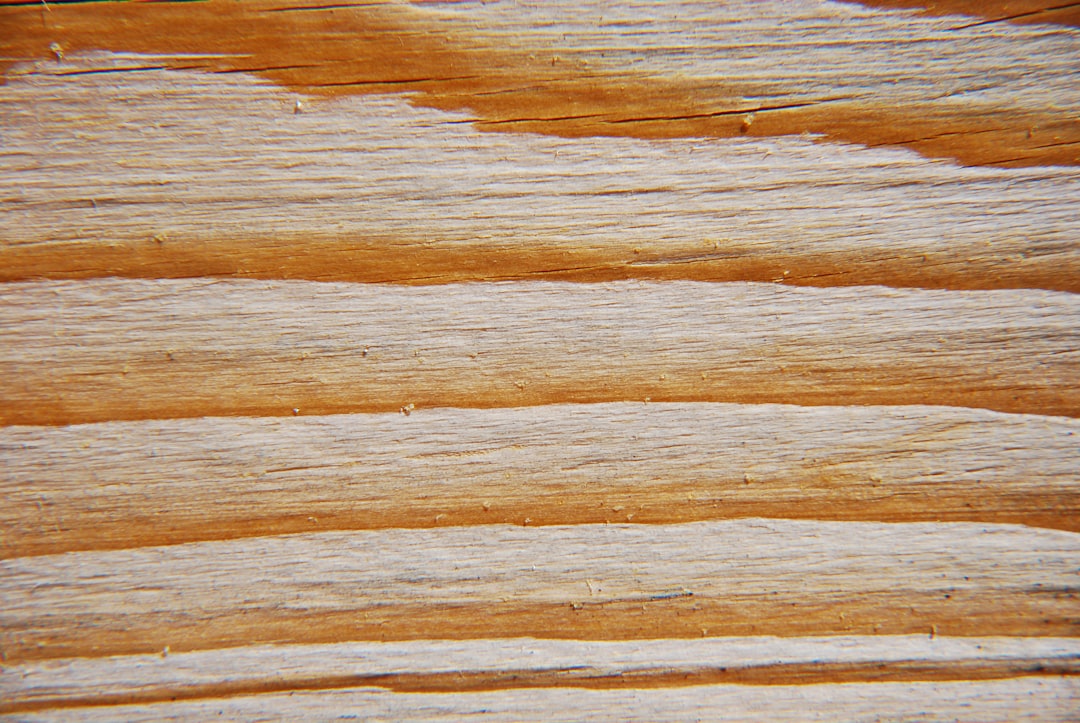 Close-up of a wooden surface showing distinct horizontal grain patterns in shades of brown and beige. The texture is rough with natural lines and variations typical of unfinished or lightly sanded wood.