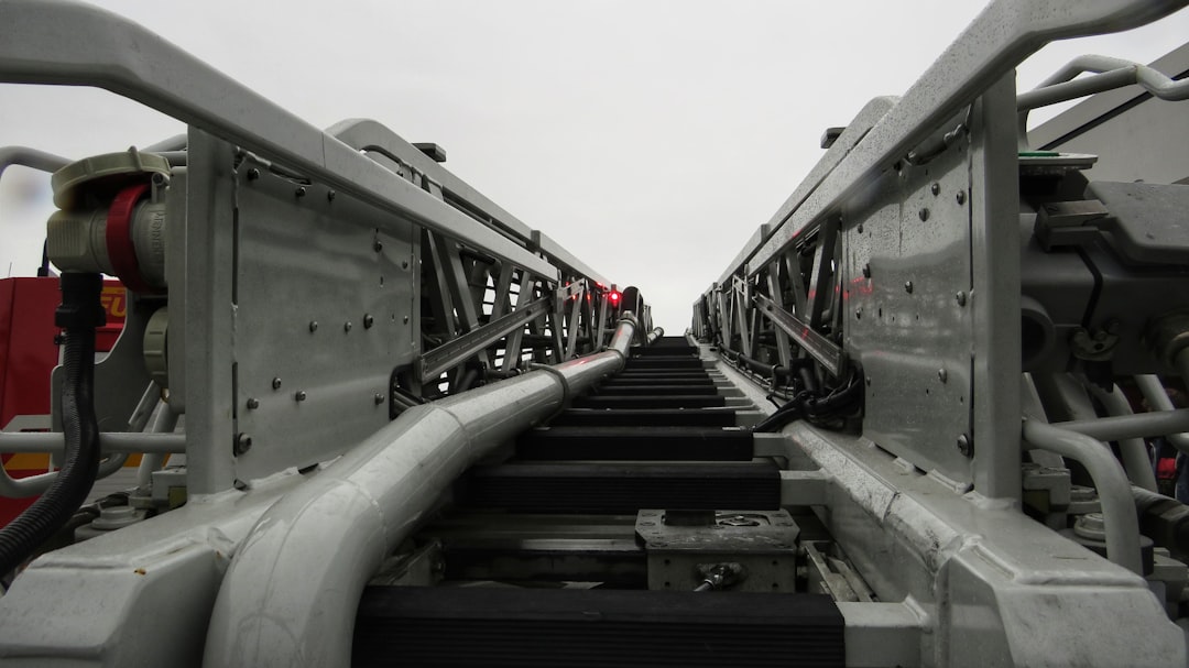 Close-up, low-angle view of a metal industrial ladder or platform with handrails and cables, leading upward toward a cloudy, overcast sky.