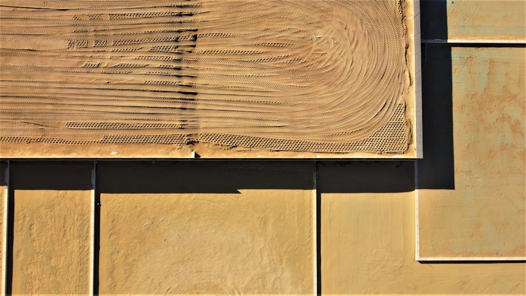 Aerial view of a sandy yellow surface with geometric panels and textured patterns, including curved tire or rake marks in the upper left section, creating an abstract design.