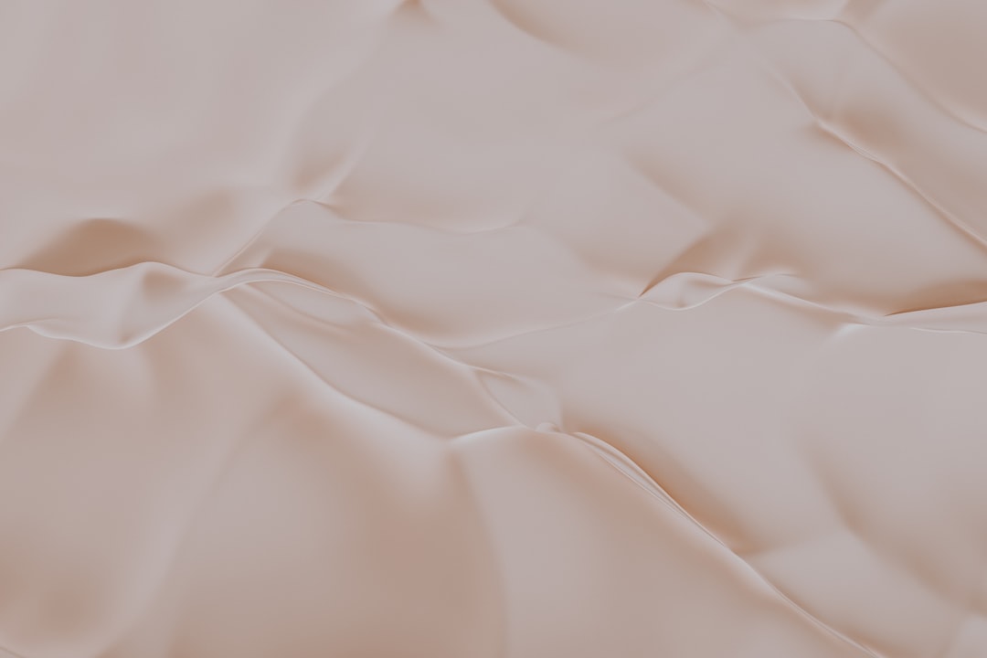 Smooth, light beige surface with soft, flowing, wavy lines and subtle folds, creating an abstract, silky texture.