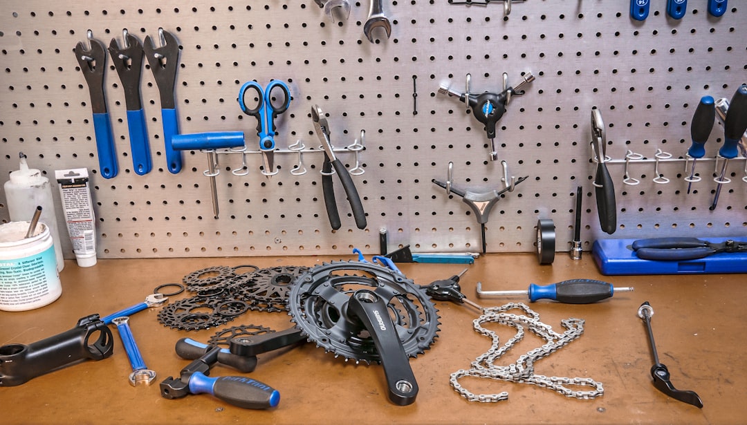 A workbench with various bicycle repair tools hanging on a pegboard, and bike parts including gears, a chain, and cranksets laid out on the wooden surface.