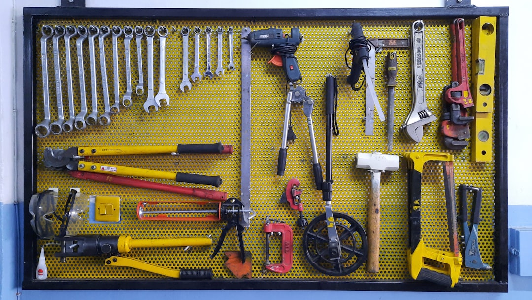 A yellow pegboard displays assorted tools including wrenches, pliers, bolt cutters, hacksaws, a hammer, a level, a drill, and various hand tools, all neatly organized and hanging in rows.