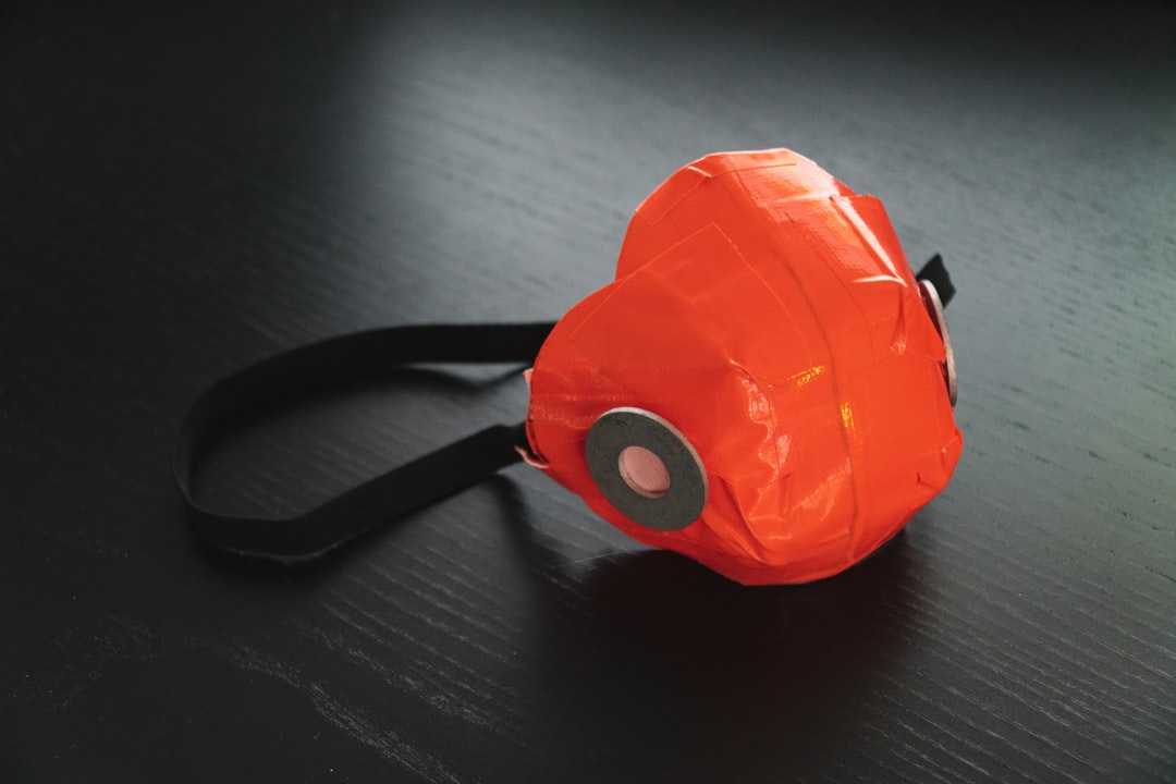 A homemade face mask made of bright orange material with black elastic straps and a circular filter, placed on a dark surface.