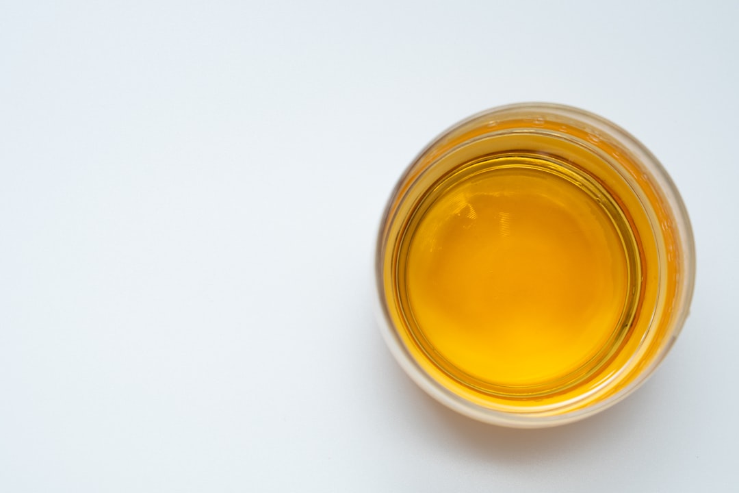 A top-down view of a glass filled with golden yellow liquid, placed on a plain white surface with ample empty space around the glass.