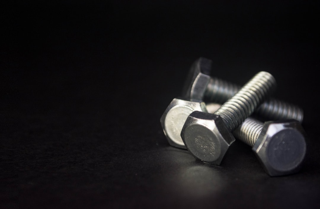Three silver hex bolts are placed on a dark, smooth surface with a black background. The bolts are arranged closely together, with their heads facing forward and the threads extending to the right.