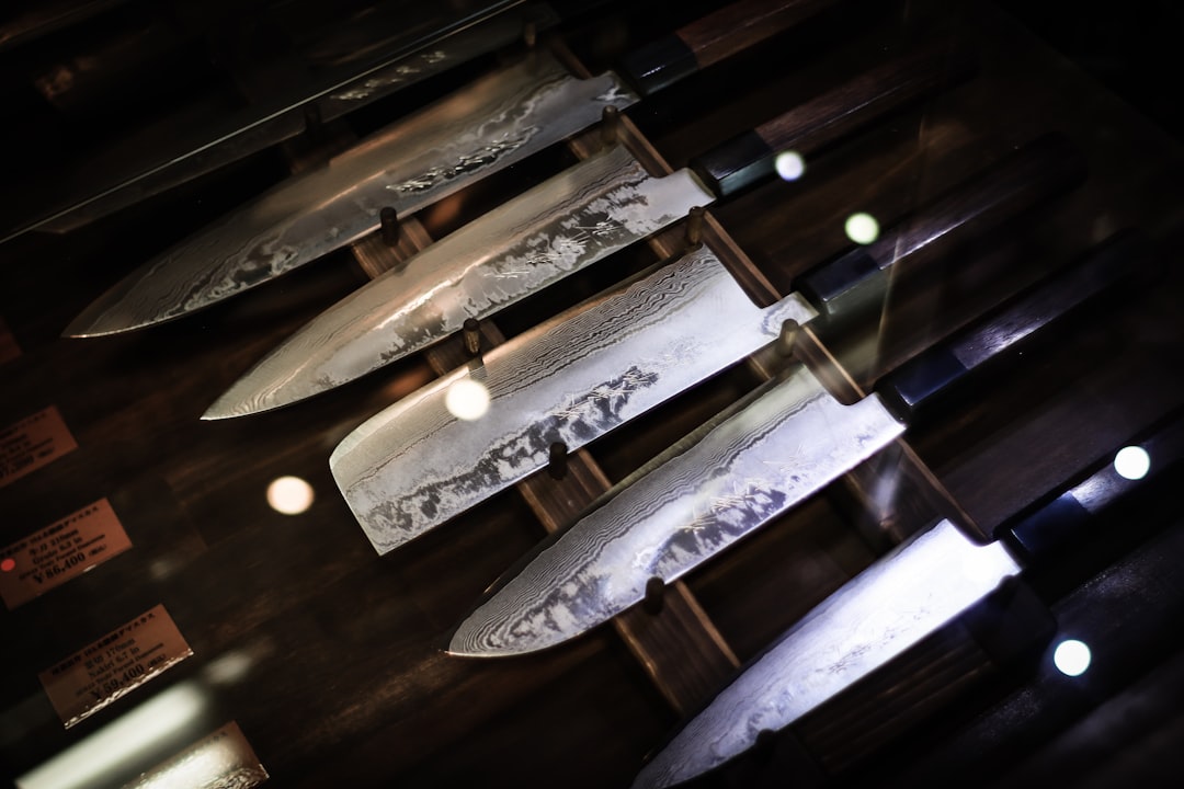 A display of several large, polished kitchen knives with wooden handles, arranged neatly on a wooden rack; light reflections are visible on the blades.