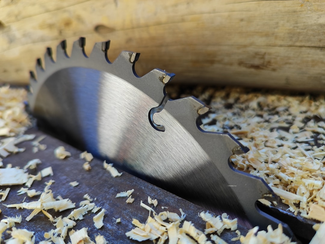 A circular saw blade partially embedded in a wooden surface, surrounded by wood shavings, with a log in the background.