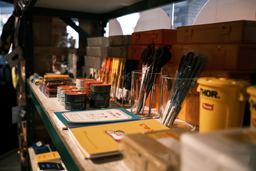 A shelf in a store displaying various stationery items, including pencils, pens, scissors in cups, notebooks, yellow storage boxes, and other colorful office supplies neatly arranged.