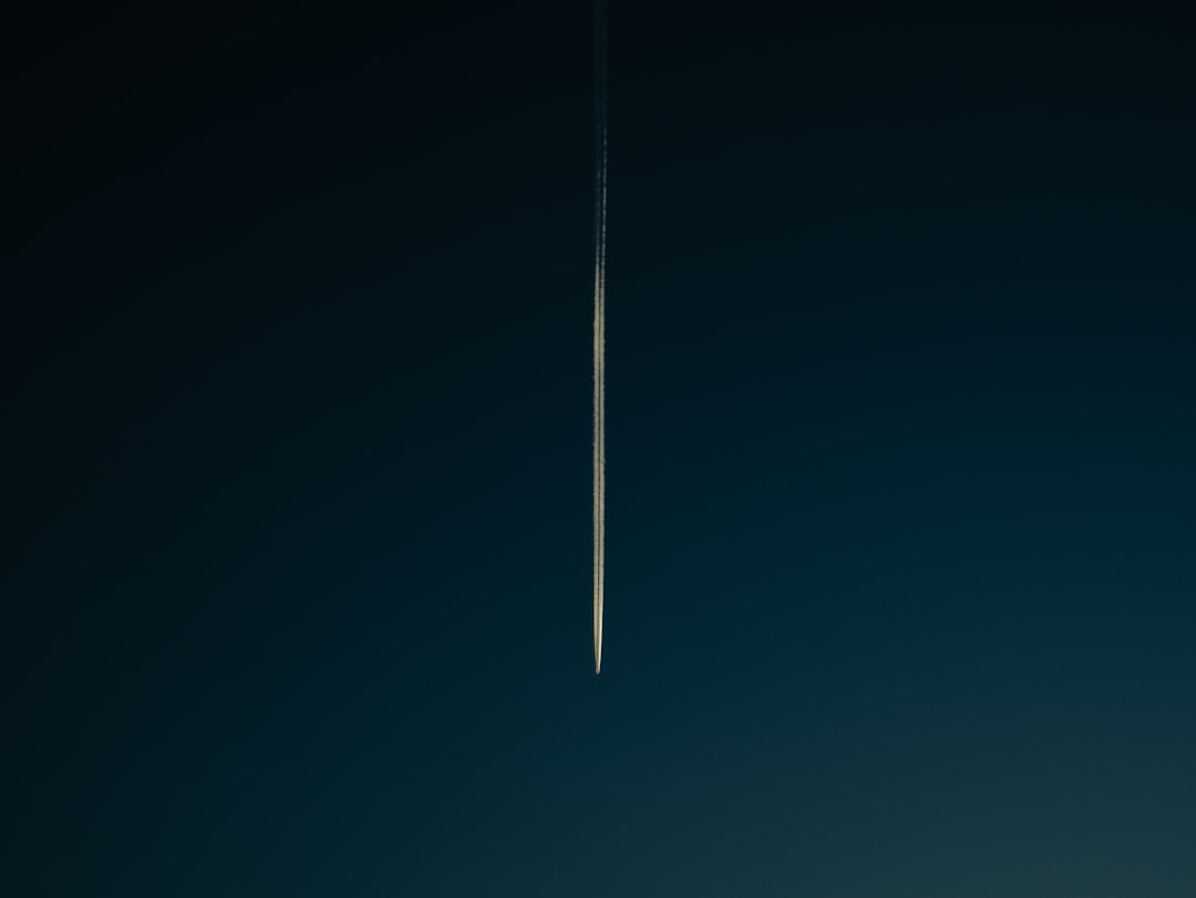 A jet leaves a thin, white contrail streaking vertically upward against a deep, dark blue sky.